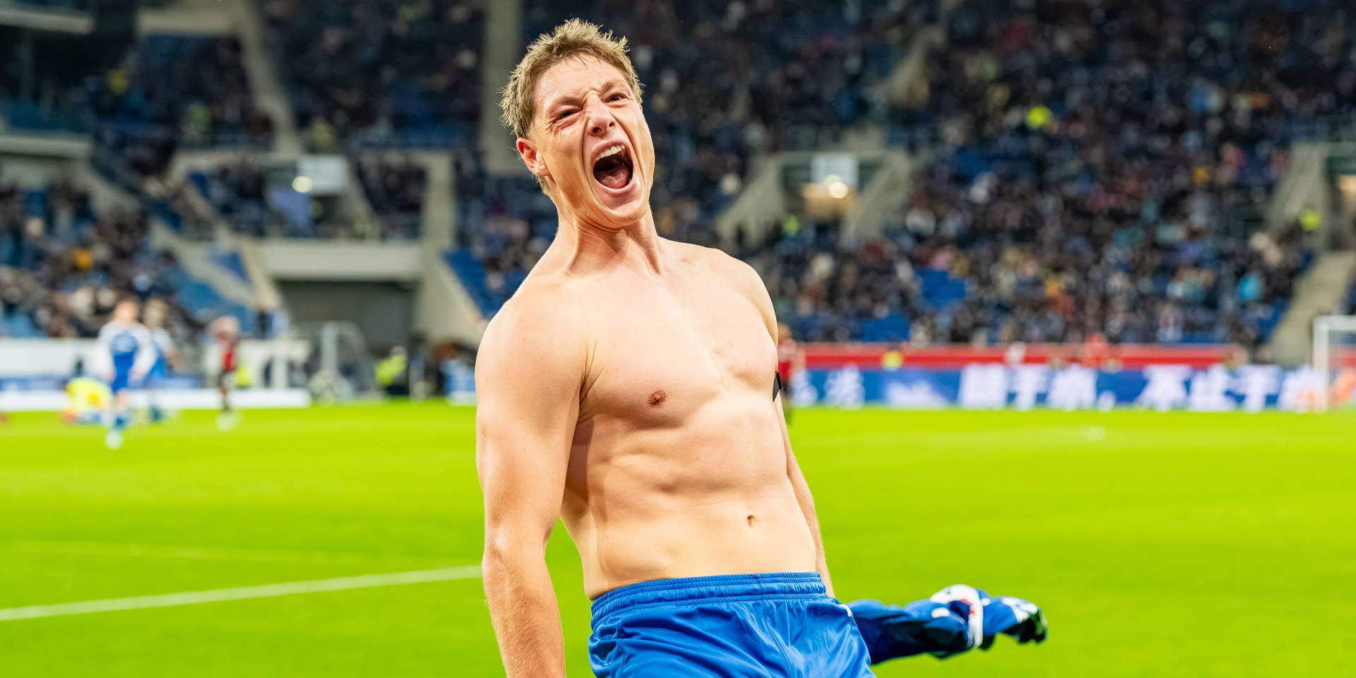 Ein jubelnder, oberkörperfreier Fußballspieler feiert auf dem Spielfeld ein Tor im Stadion.