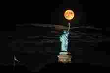 sturgeon supermoon breaks through clouds above statue of liberty, liberty state park, new jersey, august 2023