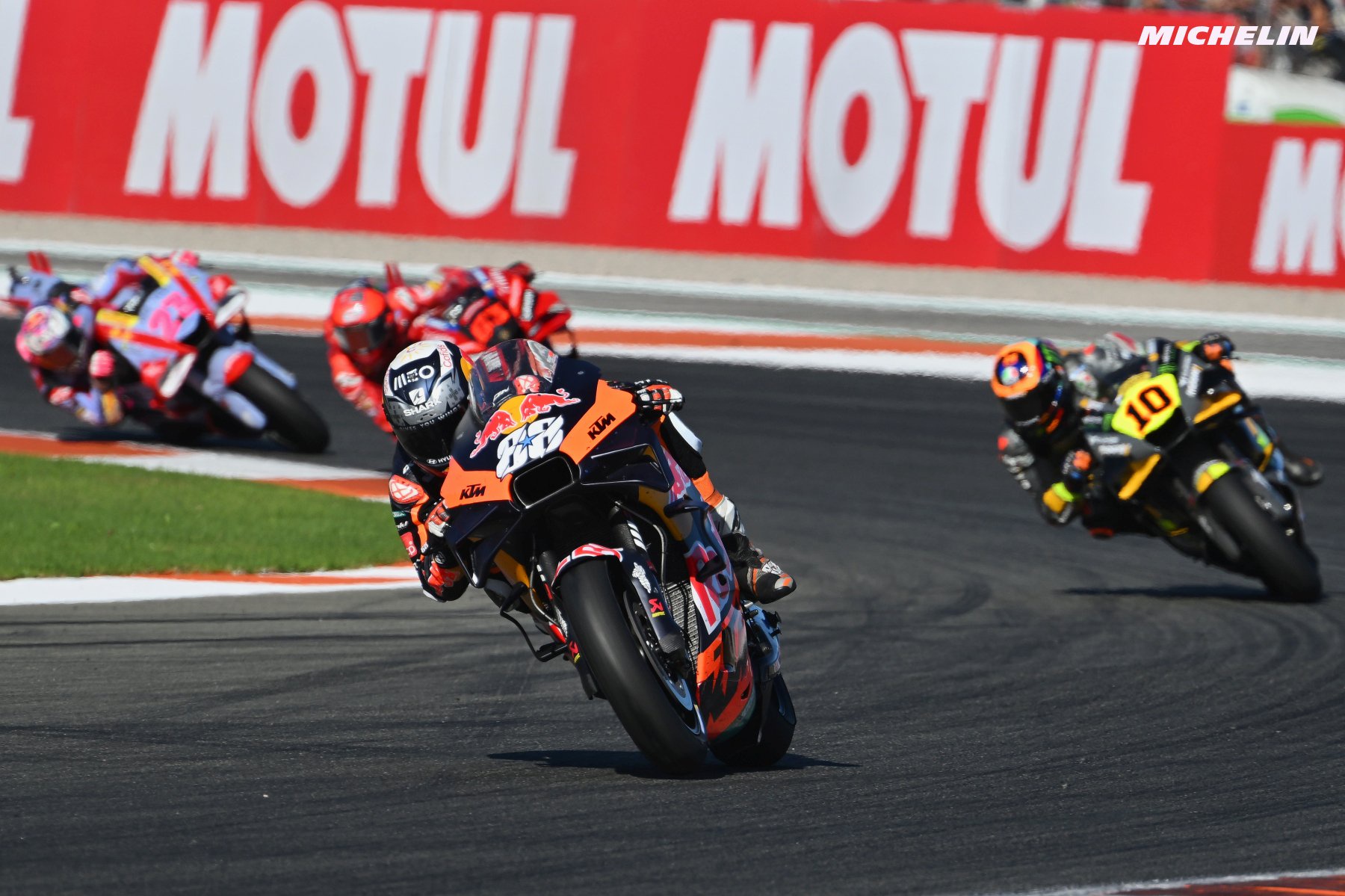 KTM rider in orange-and-black livery, number 88, leading on track at a MotoGP race with Motul banners behind.