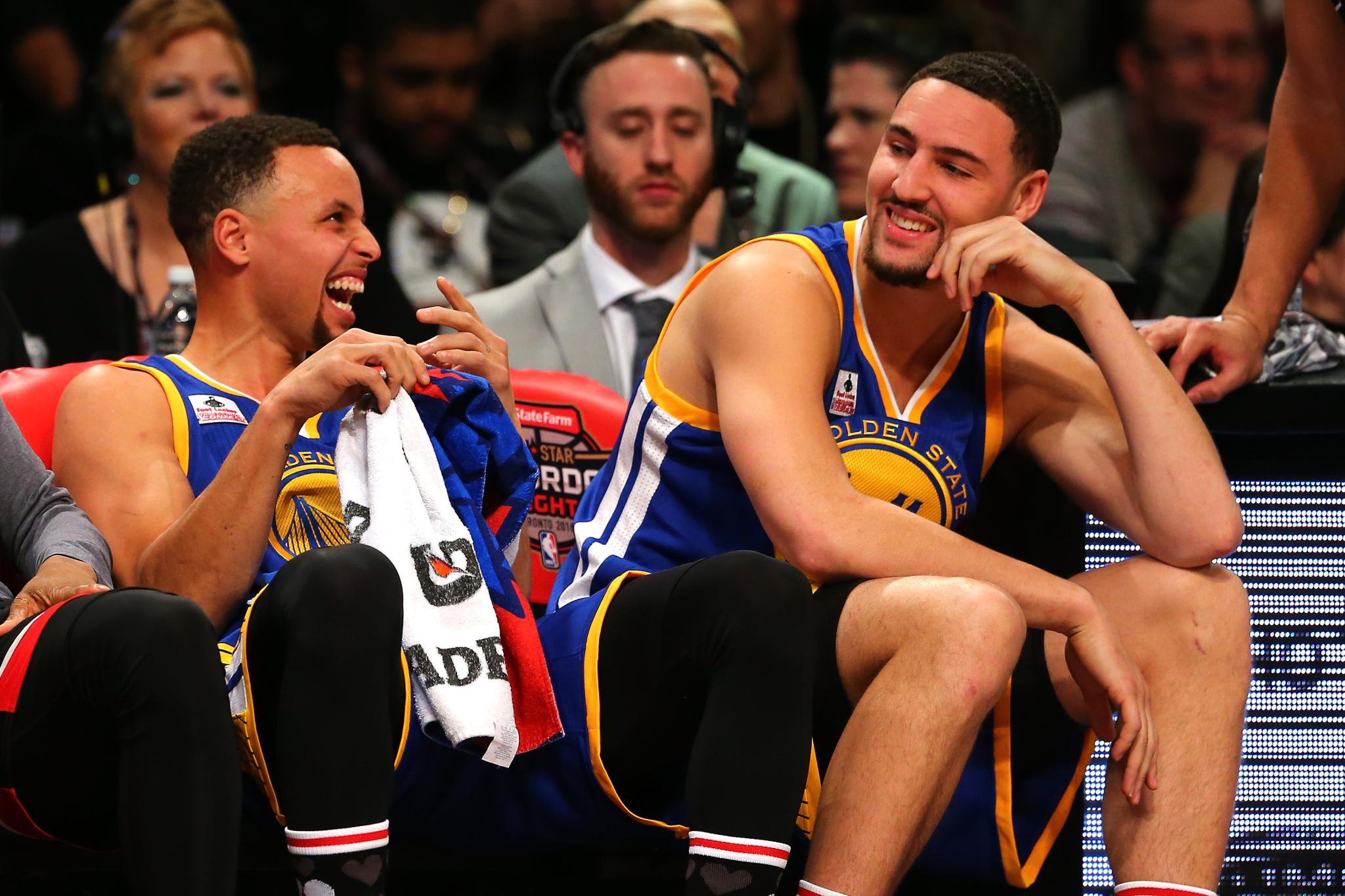 Stephen Curry and Klay Thompson sitting on the bench laughing during the Foot Locker Three-Point Contest.