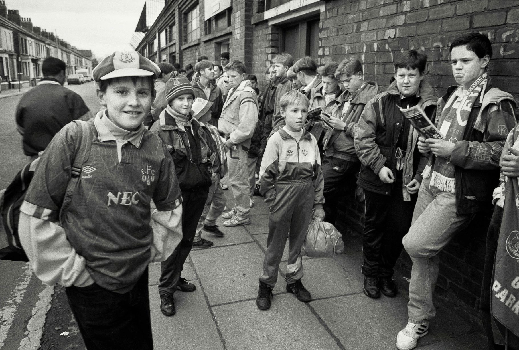 In 1991, photographer Richard Davis followed supporters from across the North West for a book about football, fashion and music. Richard spent much of the season taking pictures of fans from Liverpool, Everton and more for the book Football With Attitude. In collaboration with Lower Block, the Going to the Match zine has been published to coincide with an exhibition of the same name at Bury Art Museum, running from October 2024 to March 2025.
Pictured: Everton Fans at Goodison Park in 1991
