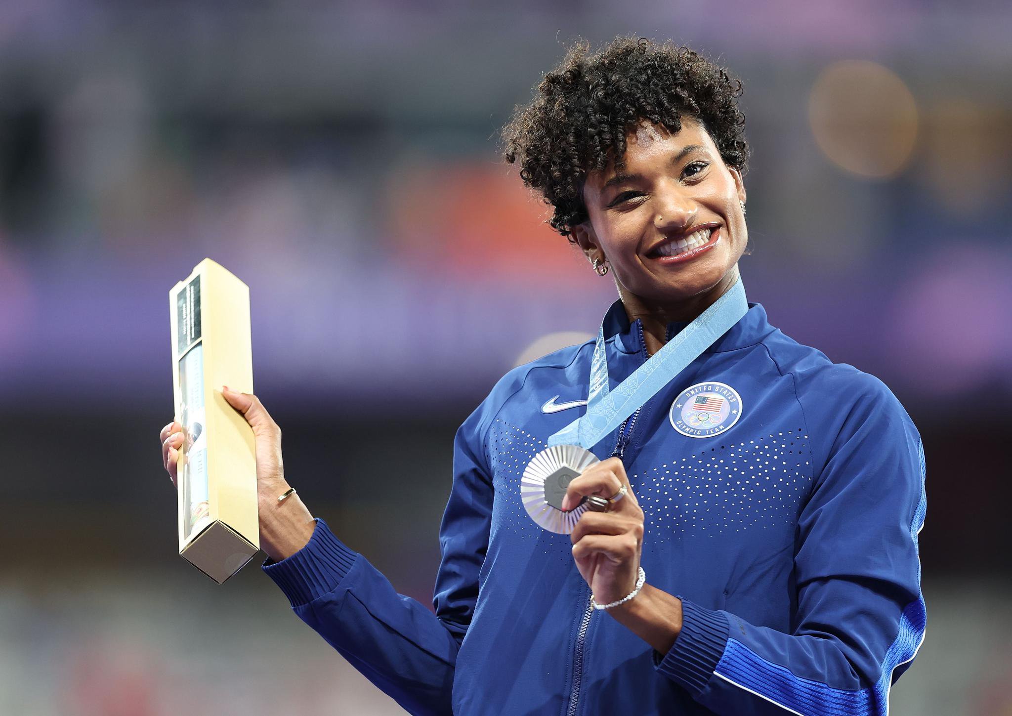 US athlete Anna Cockrell smiles while holding her silver medal and a commemorative poster tube after the women's 400m hurdles at the Paris Olympics.