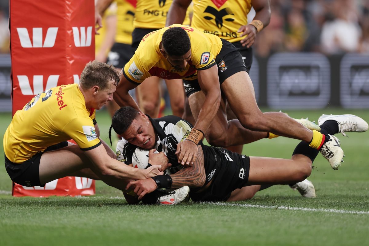 Rugby players in yellow and black jerseys tackle a player in a black and white jersey, holding a ball.