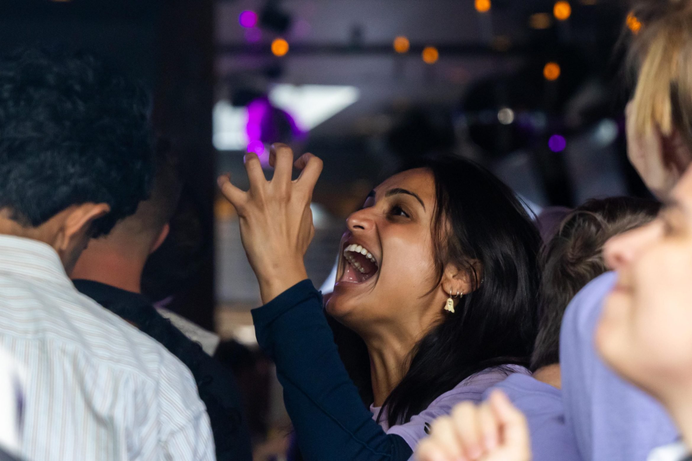 A woman in a crowd with her mouth open and hand raised, looking excited.