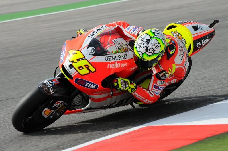 Rider in red-and-white Ducati leathers, number 46 on the fairing, leaning into a corner on a Ducati MotoGP bike at speed