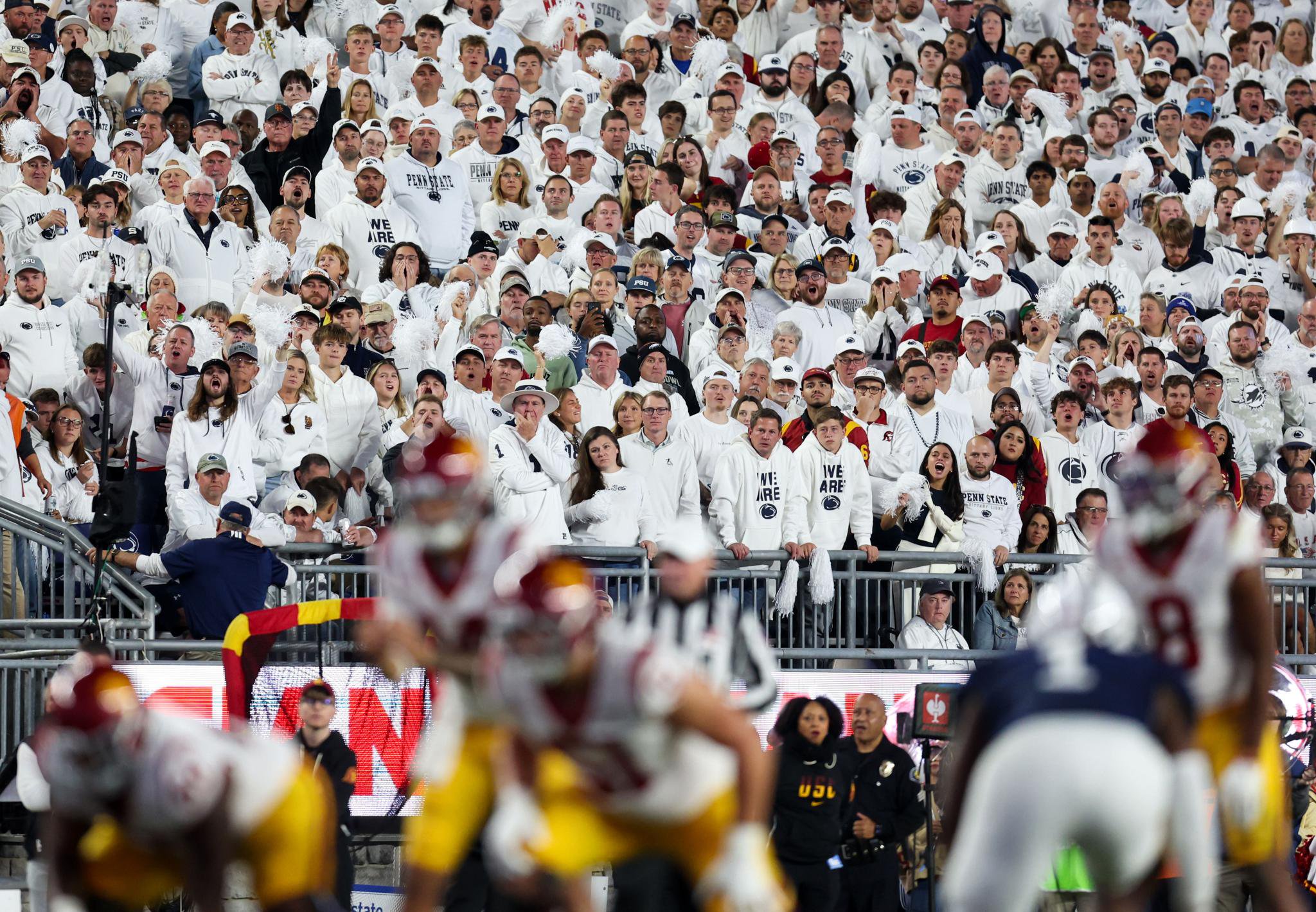 A packed stadium of Penn State fans in white clothing, with Southern California players in the foreground.