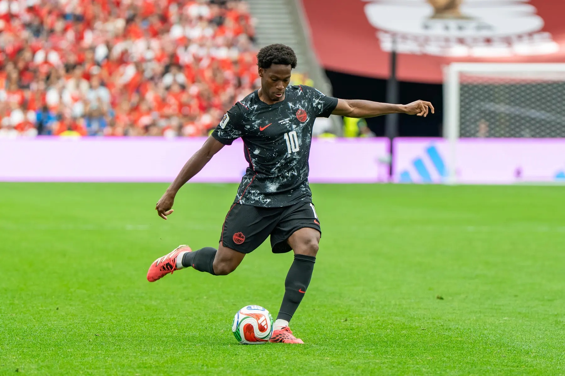 Jonathan David in a black Canada national team kit kicking a football during a match.
