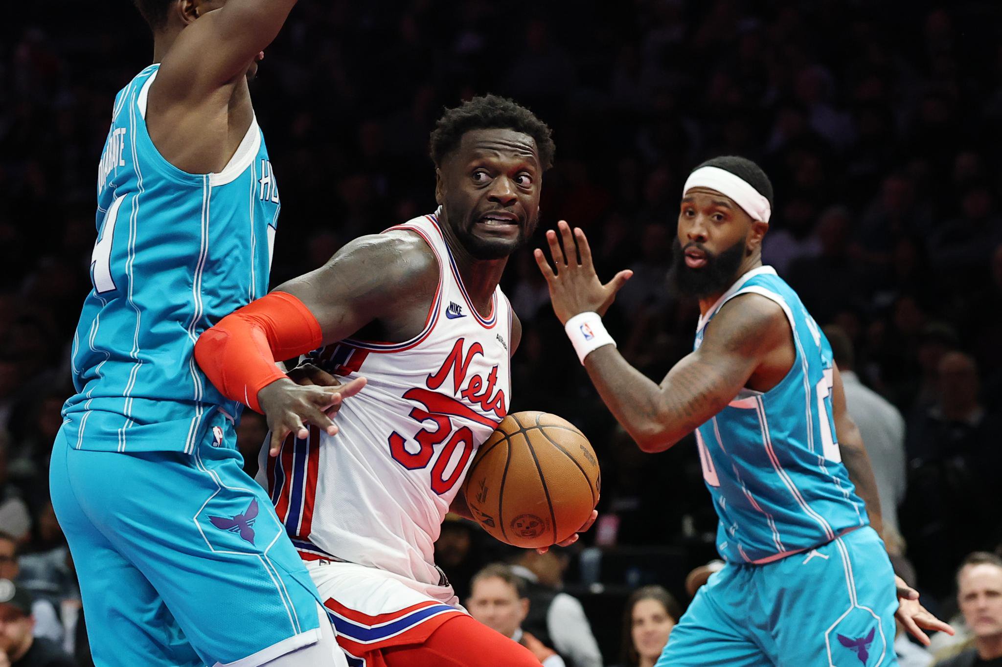 Julius Randle of the Brooklyn Nets looks to pass as Moussa Diabate and Royce O'Neale of the Charlotte Hornets defend.