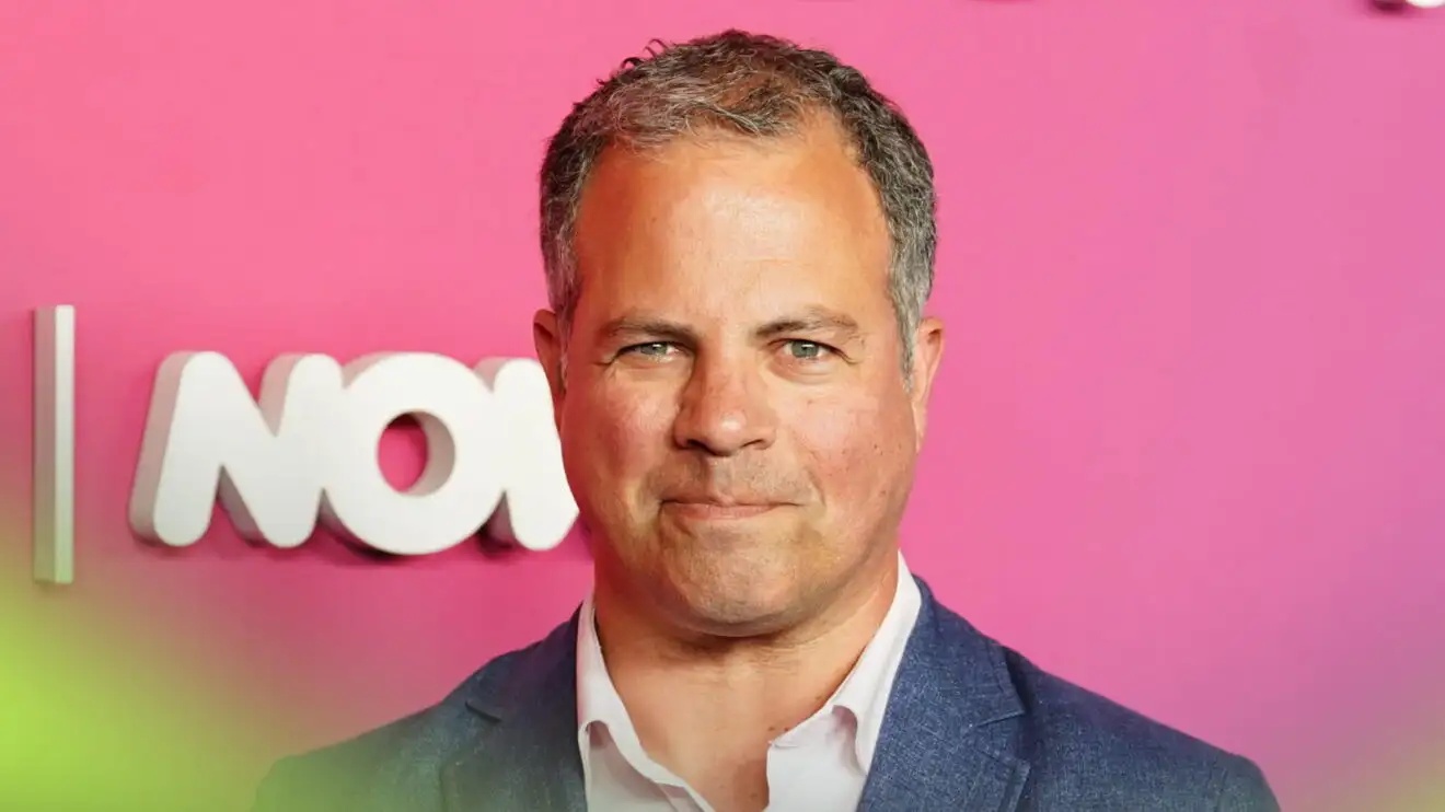 Ted Kravitz directly eyes the camera while wearing a suit against a bright-pink background