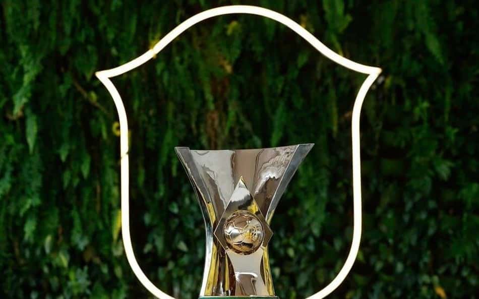 Troféu do Brasileirão com esfera dourada no centro, diante de escudo iluminado ao fundo.