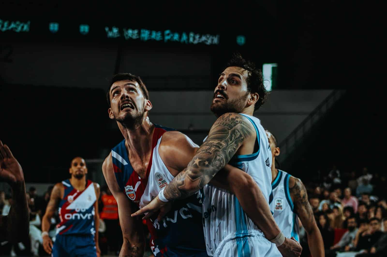 Two basketball players battle for position near the basket during an indoor game