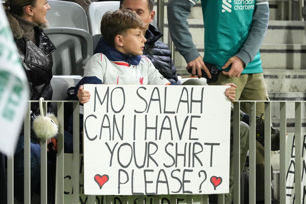 A young fan holds a sign that reads, "Mo Salah can I have your shirt please?" with a heart drawn on either side.