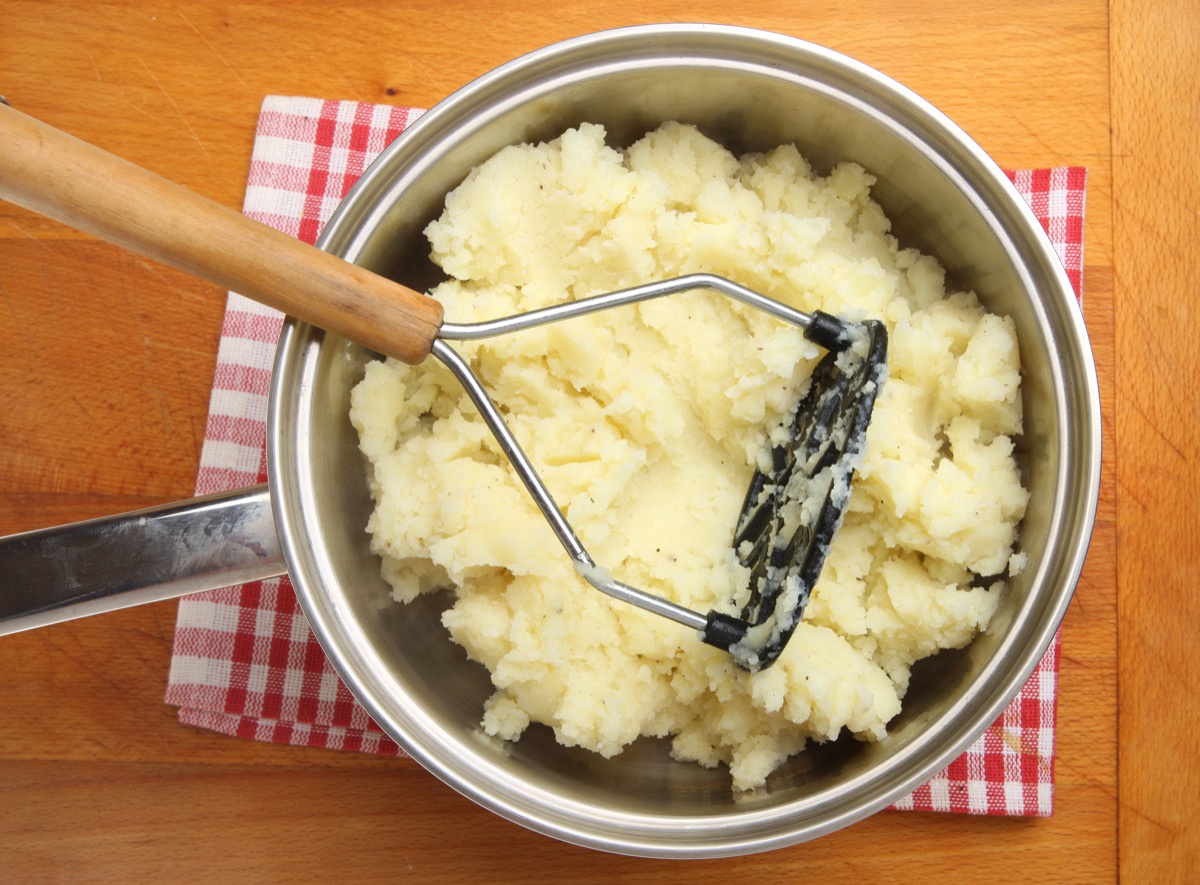 silver pot with mashed potatoes and potato masher
