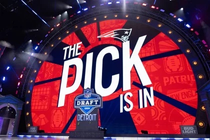 Compensatory Picks 2026 - On a large stage with a circular LED screen, “The Pick is In” appears beside the New England Patriots logo. Football symbols decorate the background, while references to the 2024 NFL Draft in Detroit and Bud Light branding round out this exciting moment. This description was automatically generated with FootballR AI.