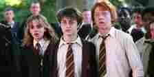 Harry, Hermione, and Ron look shocked in a crowd of students at Hogwarts in Prisoner of Azkaban