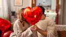 Man and woman kissing behind red hard balloon