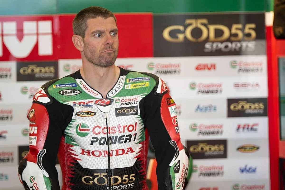 A rider in a Castrol Honda leather suit with Power1 and Go&Sport branding stands in a paddock, looking to the side in front of sponsor boards.