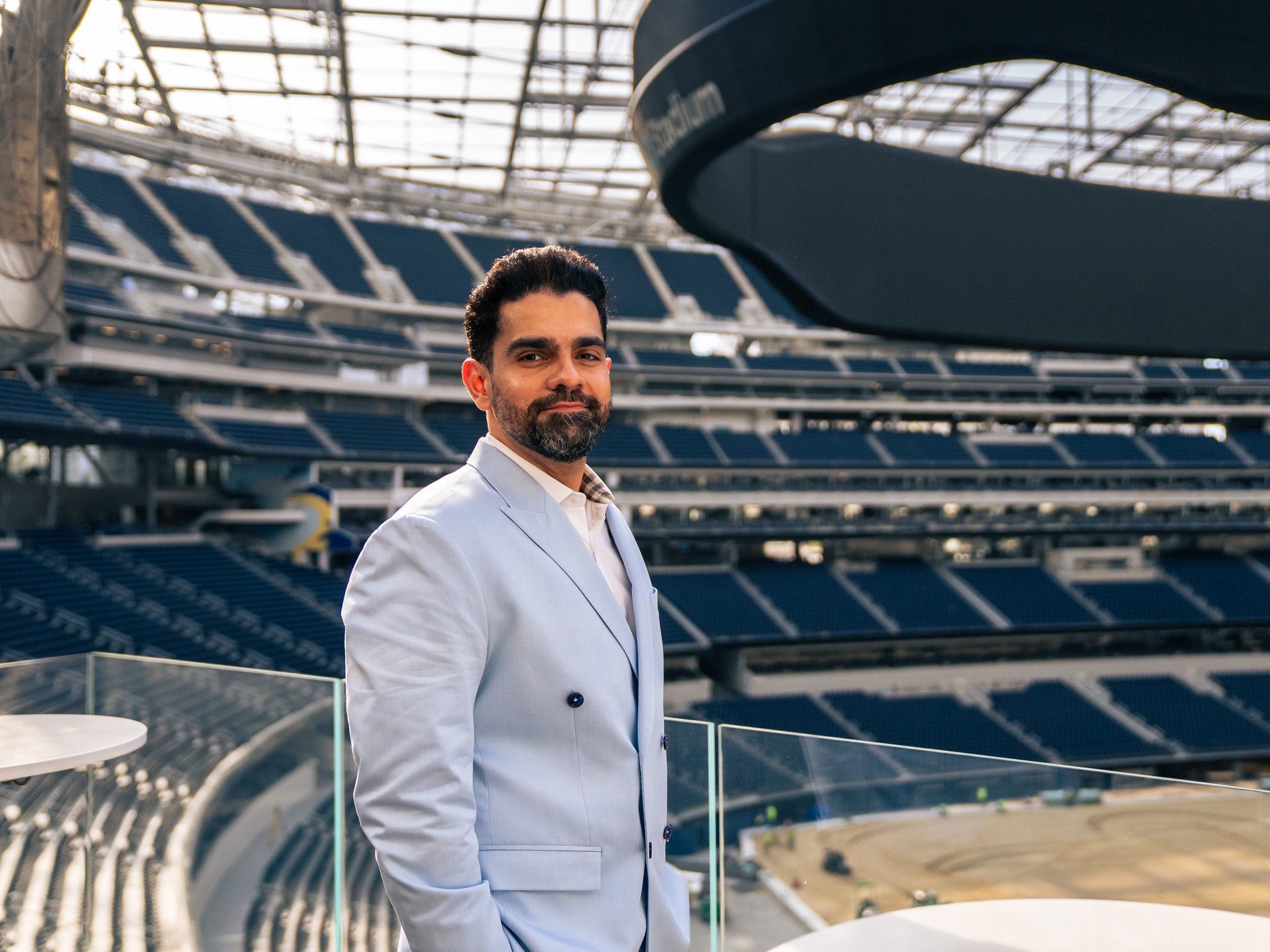 Hardik Jagda is wearing a light blue suit and standing inside a stadium.