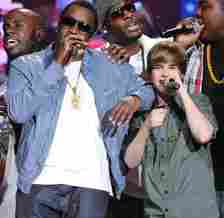 Sean 'P. Diddy' Combs, Justin Bieber, Sean Kingston, and Chris Brown on stage holding microphones to their mouths during a benefit concert in 2010