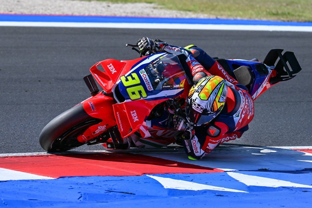 Rider in red and blue Honda leathers, number 36, leans into a corner on a red-and-white Honda MotoGP bike at a race track