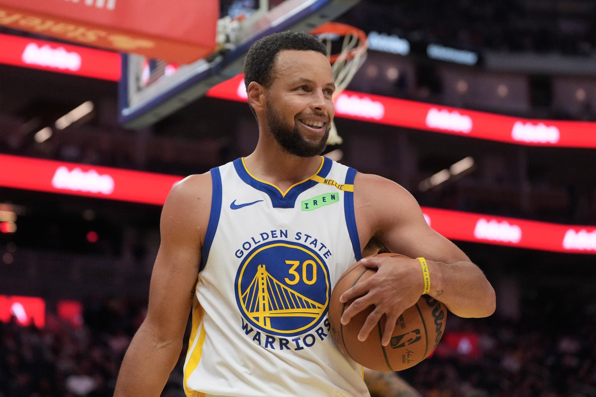 Stephen Curry smiling while holding a basketball on the court.