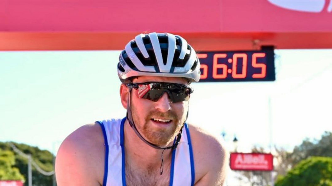 Dale Muffett, wearing a white crash helmet and a white and blue vest, smiling after the race on a pleasant day.