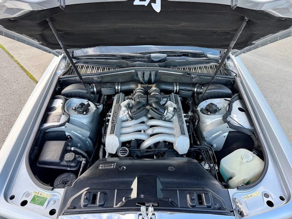 engine bay view. Exposed V12 engine with black intake components and silver valve covers.