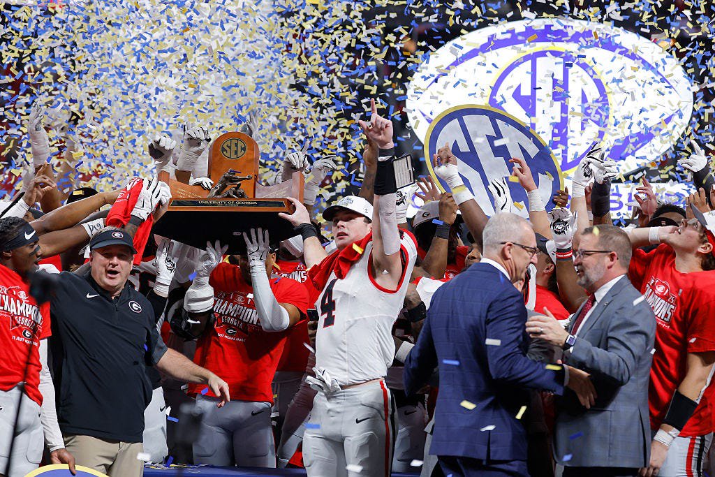 Head coach Kirby Smart and Oscar Delp (4) of the Georgia Bulldogs celebrate with teammates after defeating the Alabama Crimson Tide 28-7 in the 2025 SEC Championship at Mercedes-Benz Stadium on December 06, 2025 in Atlanta. Georgia is 11-11 in postseason games in Atlanta.