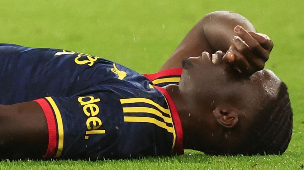 Bukayo Saka lying on grass with the back of his right hand held over his eyes