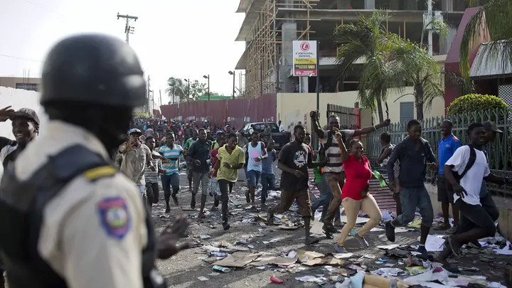A police officer looks on as a crowd enters the Delimart supermarket complex, which had been burned during two days of protests against a planned hike in fuel prices in Port-au-Prince, Haiti, Sunday, July 8, 2018. - Sputnik International, 1920, 14.12.2021