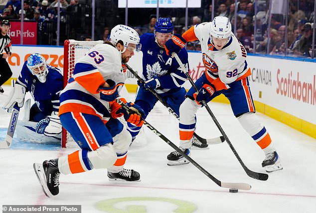 New York Islanders' Matias MacCelli (63) moves the puck as New York Islanders' Simon Holmstrom (92) and Toronto Maple Leafs' Morgan Rielly (44) look on during the first period of an NHL hockey game in Toronto, Saturday, Oct. 17, 2026. (Frank Gunn/The Canadian Press via AP)