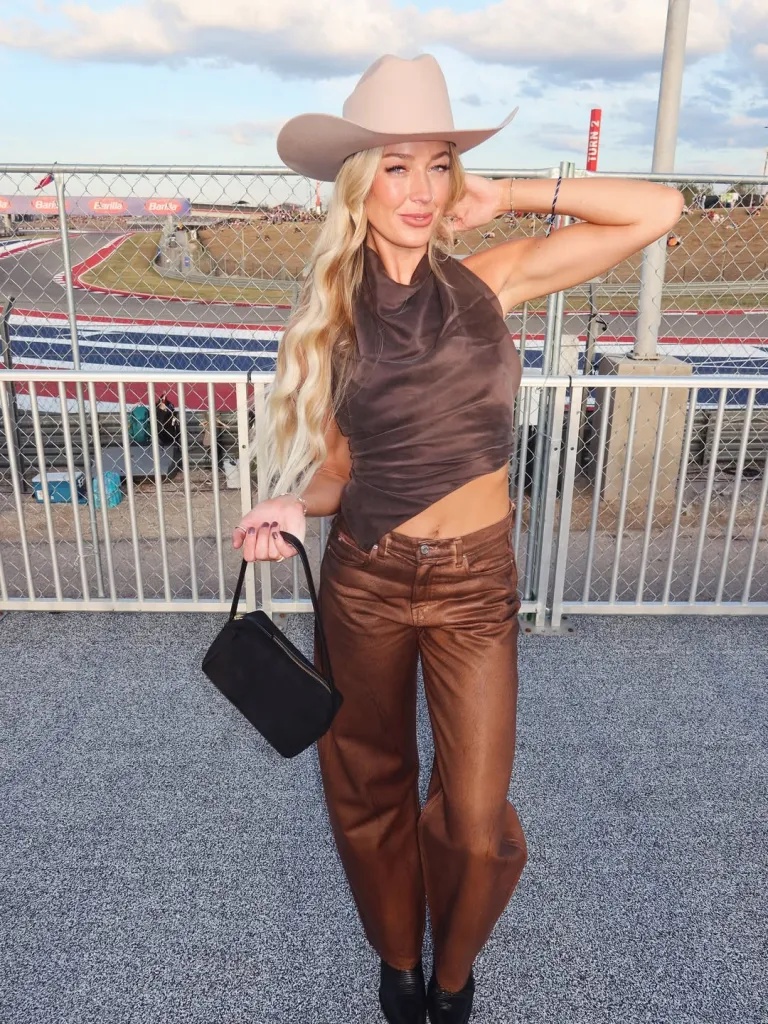 Sophie Cunningham poses in a brown halter top, metallic pants, and a cowboy hat at a racetrack.