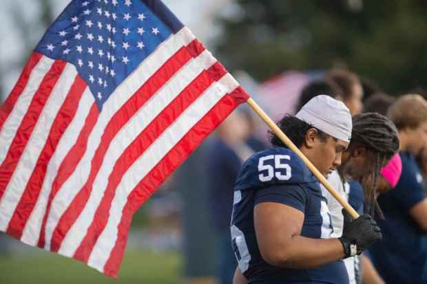 Aquinas' Sosaia Aluesi, (#55), holds an American flag and bows his head during a prayer before the start of their game against San Jacinto, at Aquinas High School in San Bernardino on Friday, September 25, 2026. (Photo by John Valenzuela/Contributing Photographer)