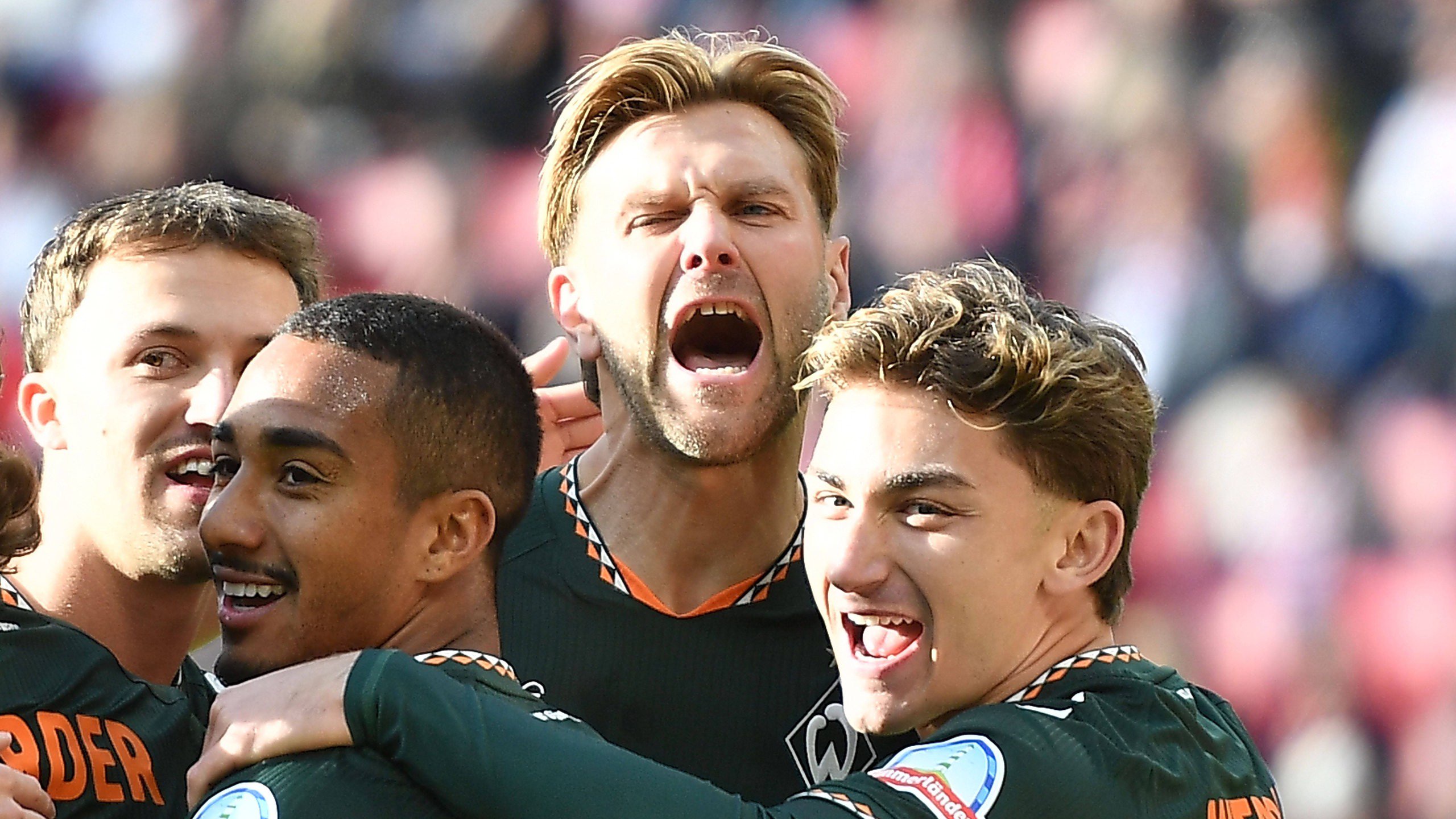 Niclas Füllkrug steht mit drei weiteren Werder-Spielern zusammen und reißt den Mund weit auf