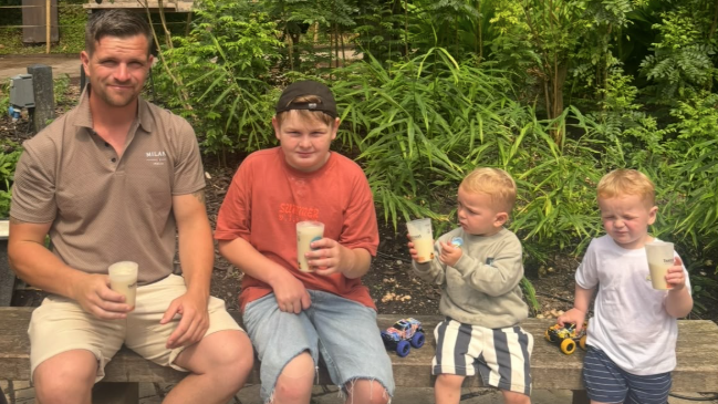 Leon and his three sons sit on a wall wearing shorts and t-shirts and holding smoothies.