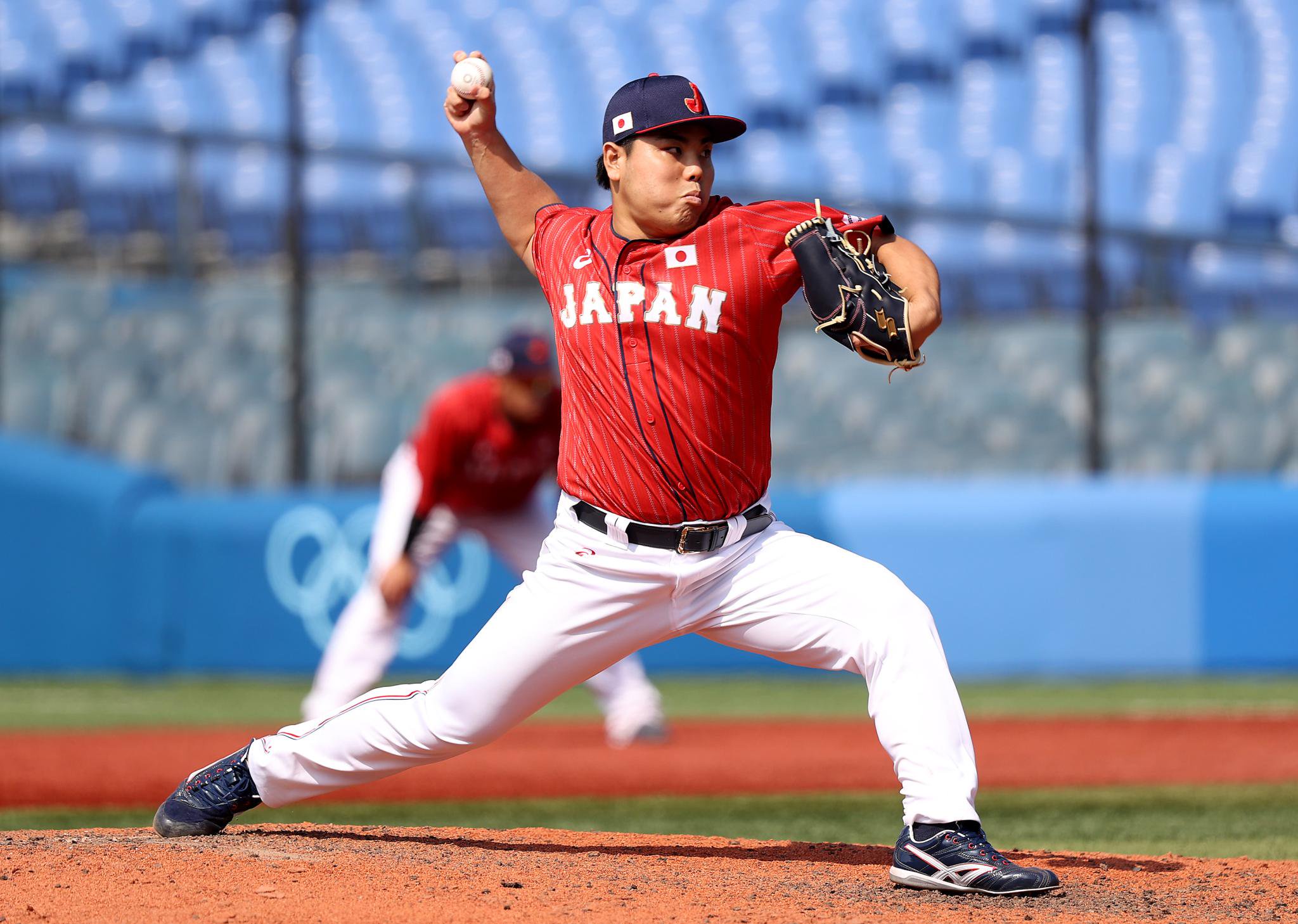 A Japanese baseball player in a red and white uniform pitches the ball during the Olympics.