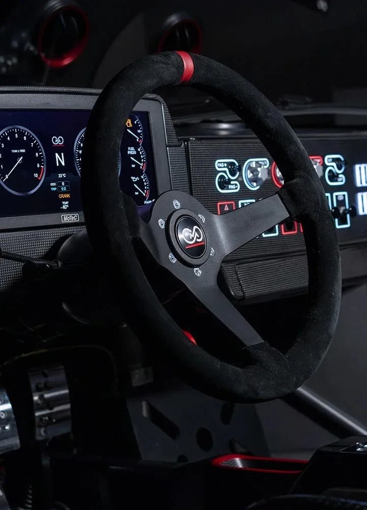 Close-up of a racing car steering wheel and dashboard with digital displays and controls.