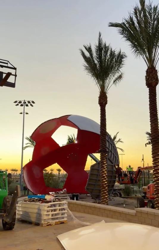Construction of a giant soccer ball sculpture at Ontario Sports Empire during sunset.