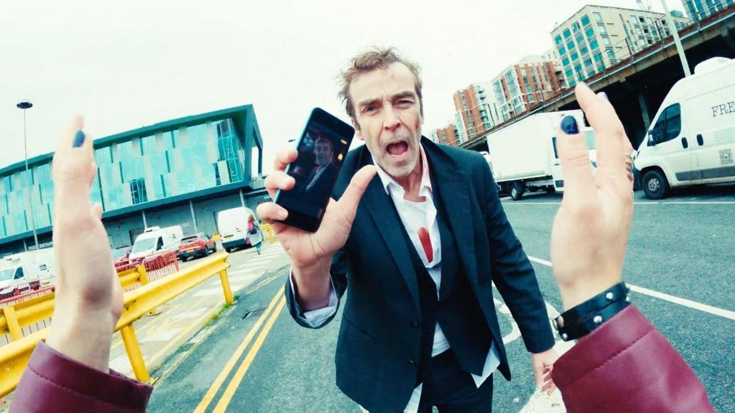 A still shot from Bad Day At The Office showing John Hannah holding up his mobile phone 