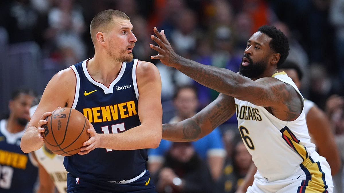 Nikola Jokić looks to pass the ball as DeAndre Jordan defends during an NBA game.