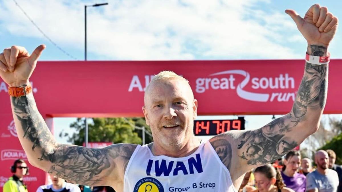 A picture of Iwan Thomas, with "Iwan" on his top, holding his thumbs up in celebration.