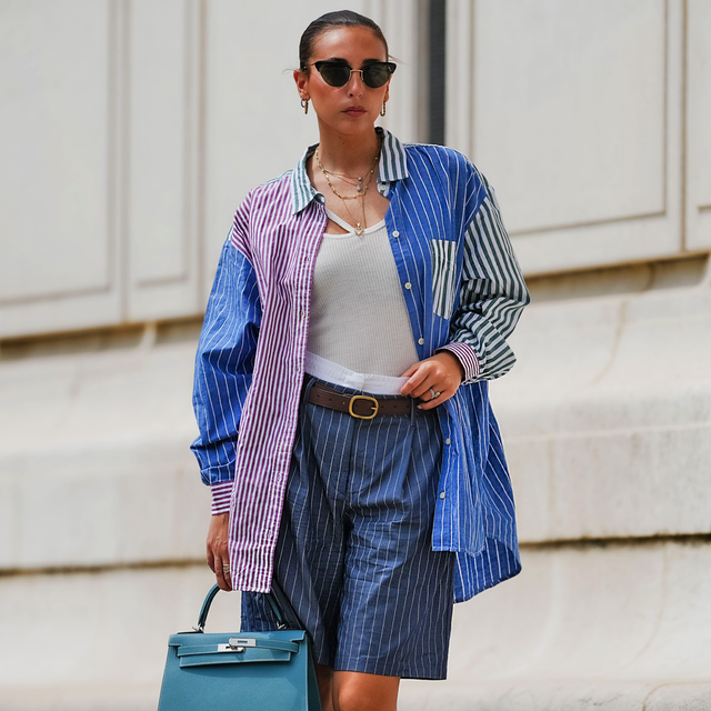 Persona que viste una camisa multicolor de gran tamaño y pantalones cortos y lleva un bolso de mano verde azulado