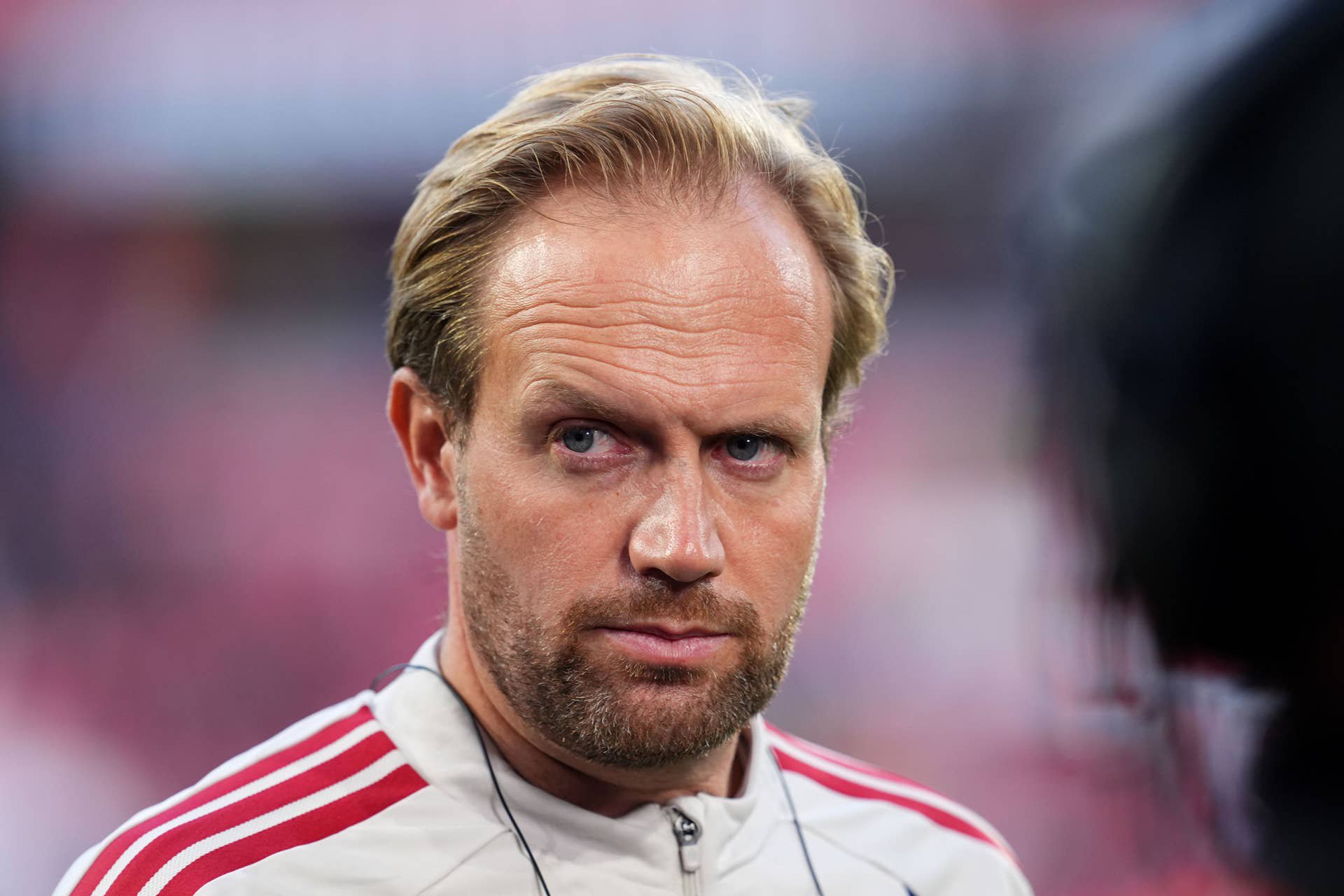 Ein Mann im Trainingsanzug blickt ernsthaft in die Kamera, unscharfer Hintergrund.