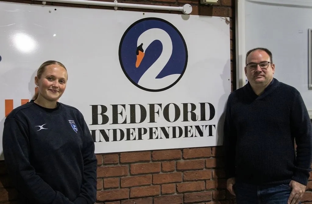 (l-r) Alivia Usher-Harris and Bedford Independent sports editor Tom Carr, beside one of the Bedford Independent boards at Goldington Road. Image: Bedford Blues Women Bedford Independent.