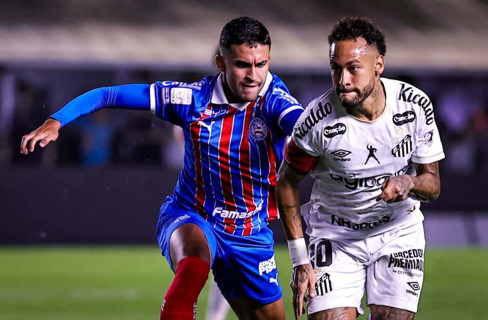 Dois jogadores disputam bola em jogo de futebol; um com uniforme do Bahia azul e vermelho, o outro branco.