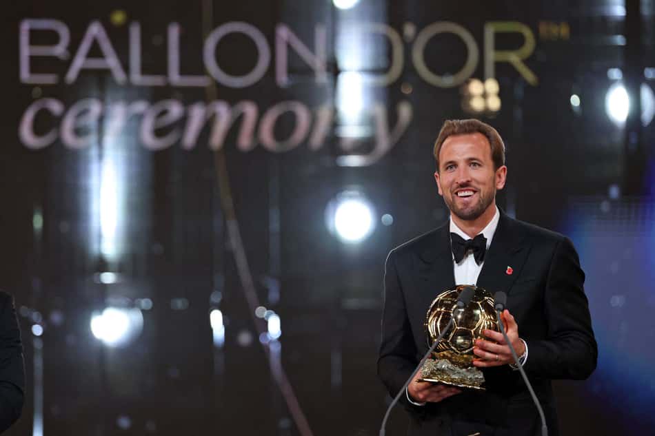 Homem de terno preto no palco segurando o troféu Ballon d'Or na cerimônia.